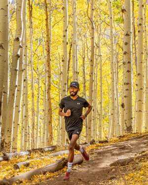 African elite athlete trail running through a yellow leafed aspen forest near Flagstaff Arizona.