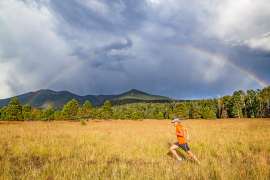 Man running in mountain meadow with a rainbow arching across the sky near Flagstaff Arizona