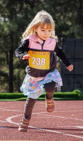 Young girl in a flower patterned skirt running toward the finish line of 400 meter dash race